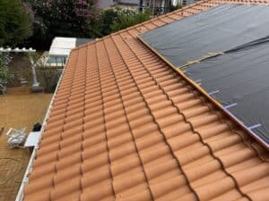 Toit en tuiles terracotta nervurées. Une zone est couverte d'une bâche noire fixée par du ruban adhésif, signalant des travaux de toiture.