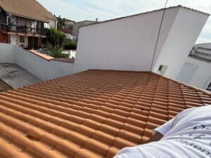 Travaux de rénovation de toiture. Gros plan sur des tuiles canal neuves orange vif, avec aperçu d'une maison méditerranéenne et son balcon.