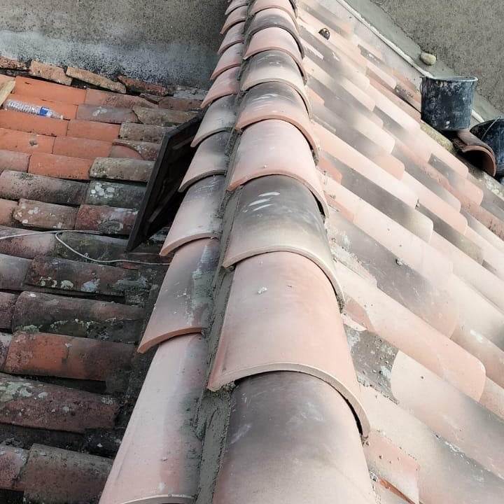 Faîtage en tuiles canal : réparation et scellement toiture Ligne de faîtage sur un toit provençal en tuiles de terre cuite anciennes, rénovée avec des tuiles canal fixées au mortier. Une ouverture est visible.