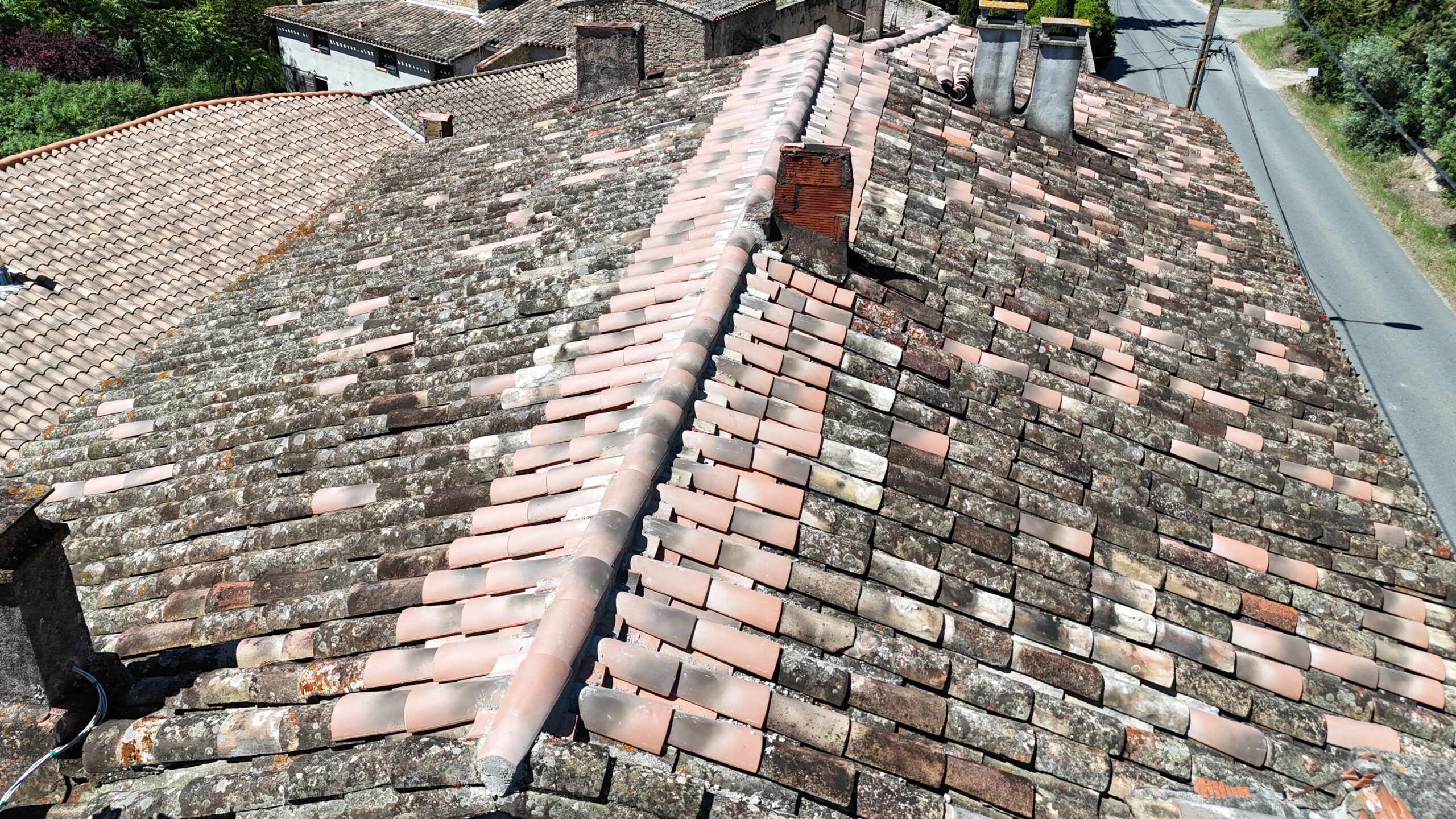 Toit ancien en tuiles canal vieillies avec faîtage et cheminée en brique, vue aérienne dans un village.